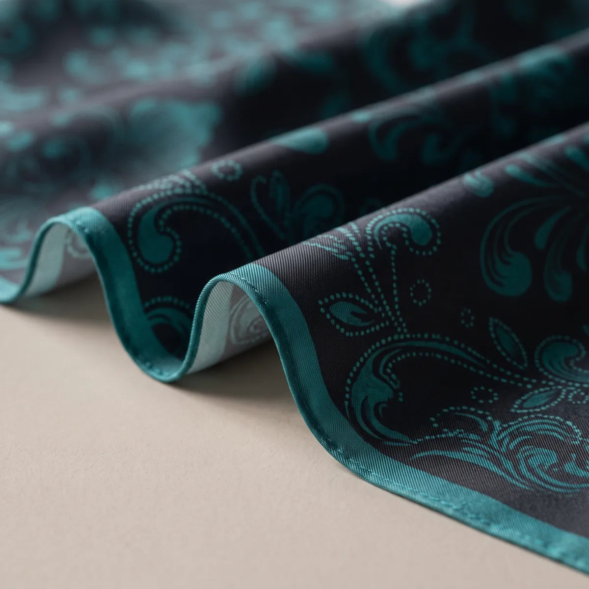 Folds of black silk printed with deep teal scrolls and dots, the dark teal hem running along the wave