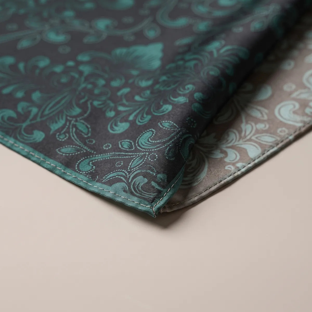 Corner of the black and dark teal bandana, ornate curls fading toward the misty reverse