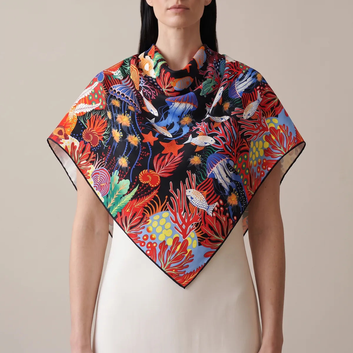 Woman in a cream dress wearing the jellyfish print silk shawl over her shoulders, the point low at the front