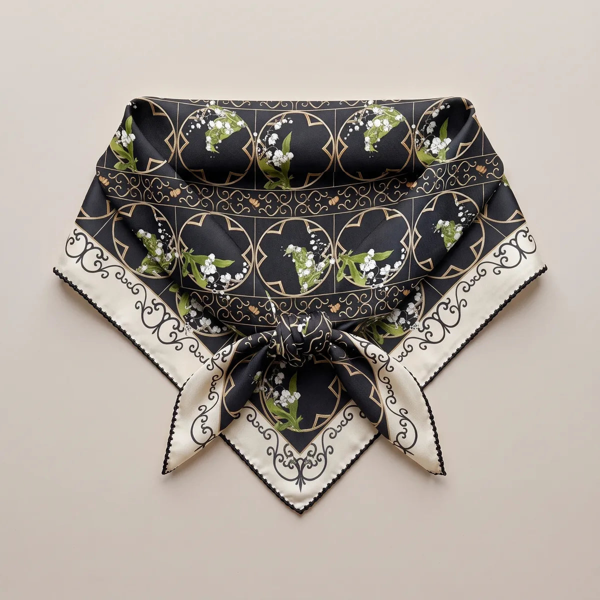 Black and cream lily print square folded and knotted, laid flat with the scroll border forming a V