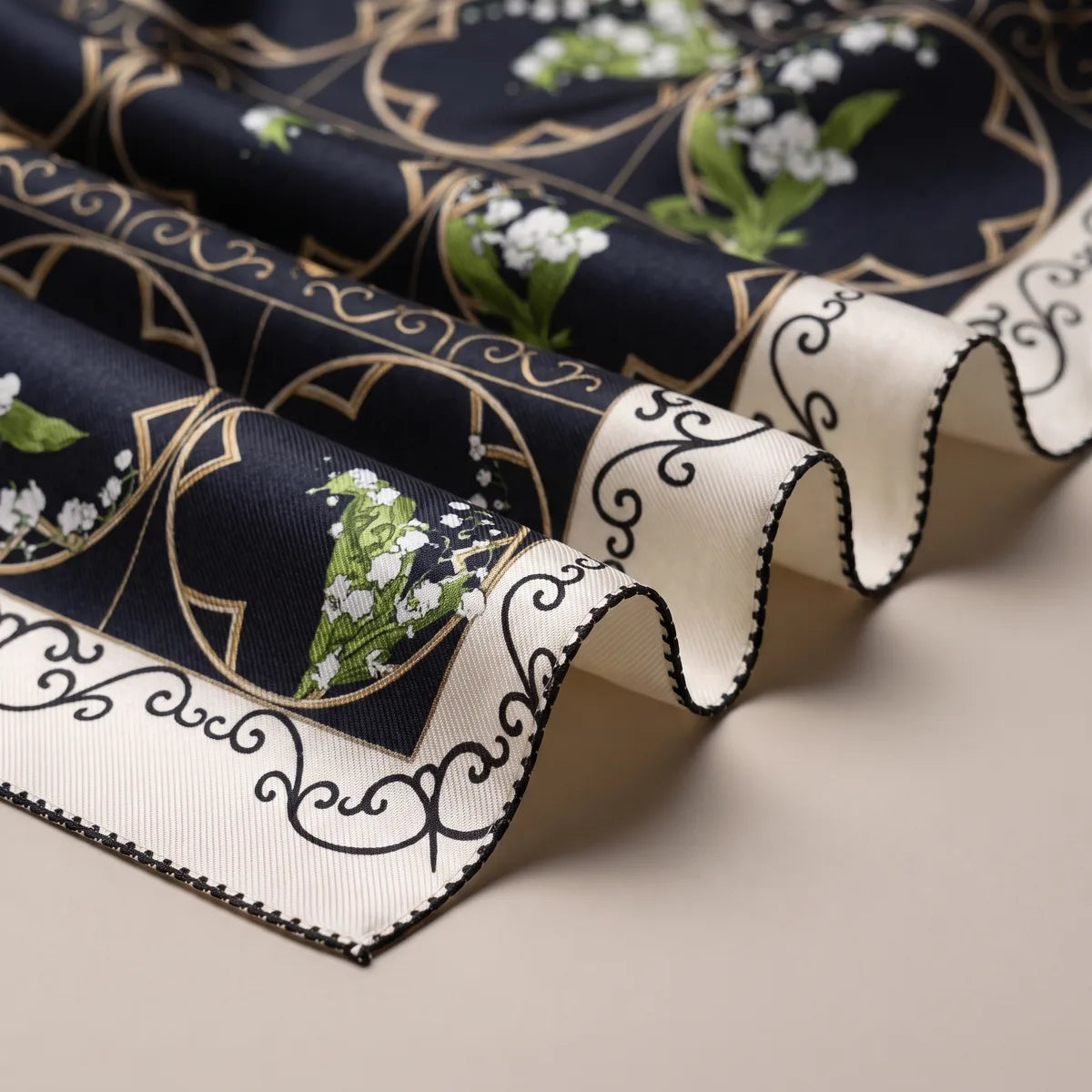 Close-up of black silk folds with lily of the valley sprigs, tan arches and the cream scroll border