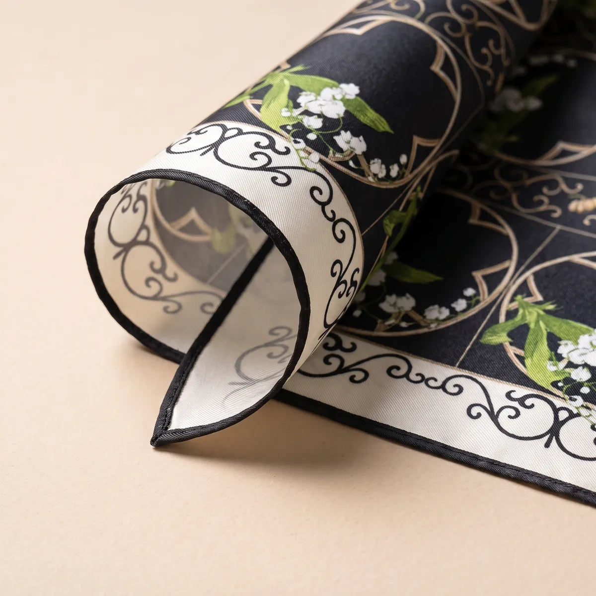 Rolled corner of the black lily scarf: the black picot-style edge, cream scrolls and a pale gray reverse