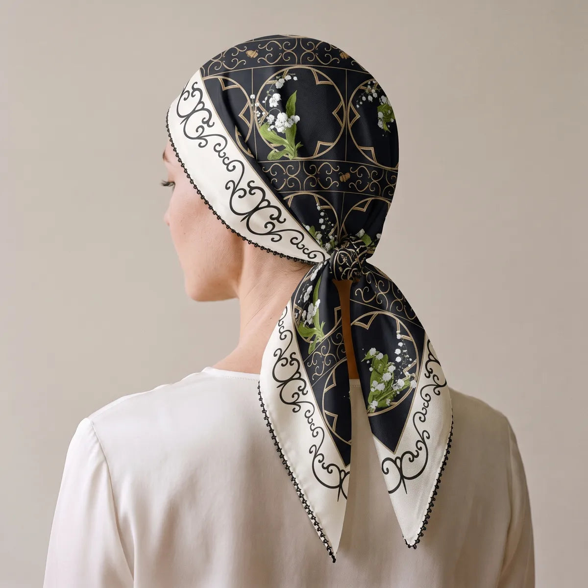 Black and cream silk scarf tied over the head and knotted at the nape, lily sprigs on the tails