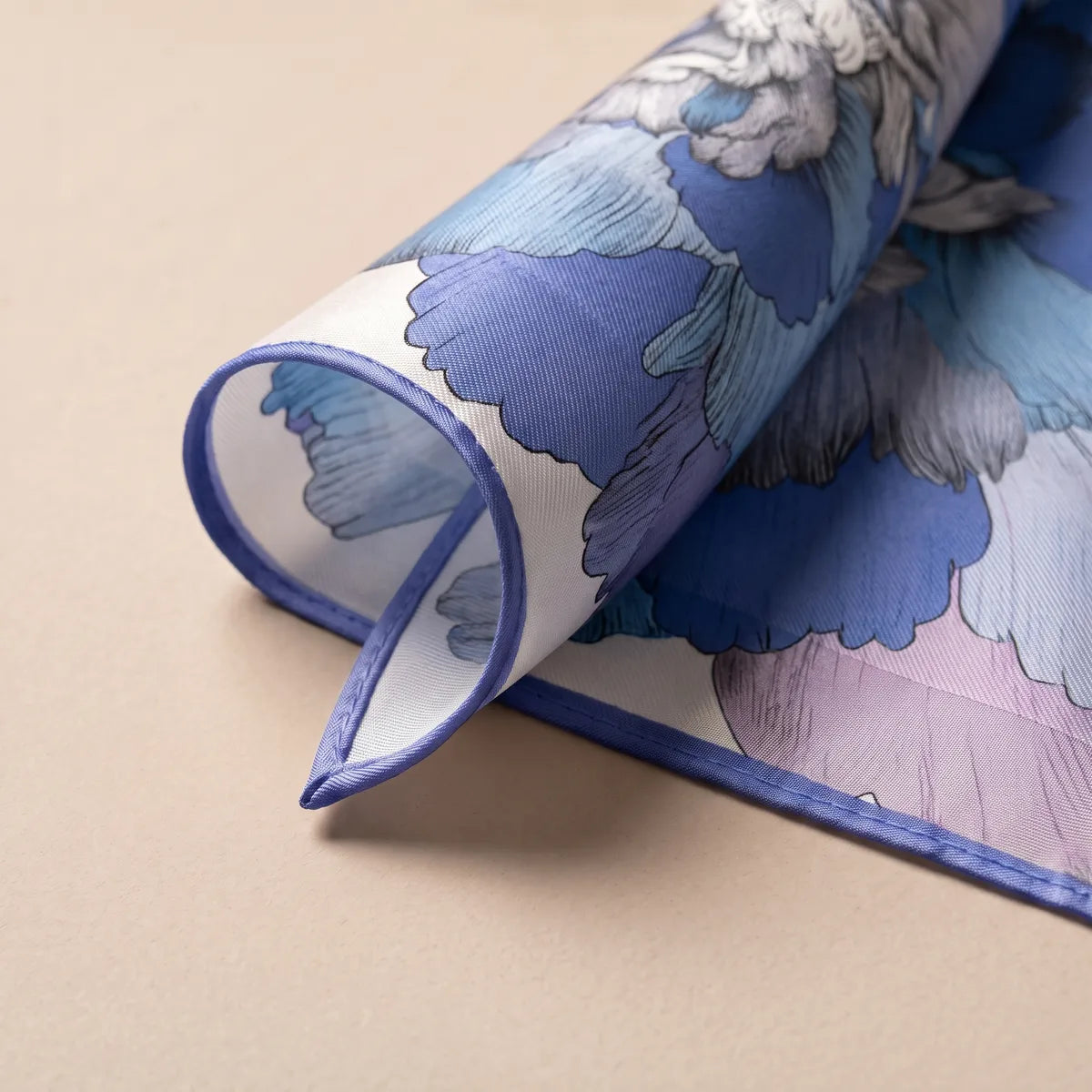Rolled corner of the blue floral scarf showing the ivory ground, the periwinkle edge and the paler reverse