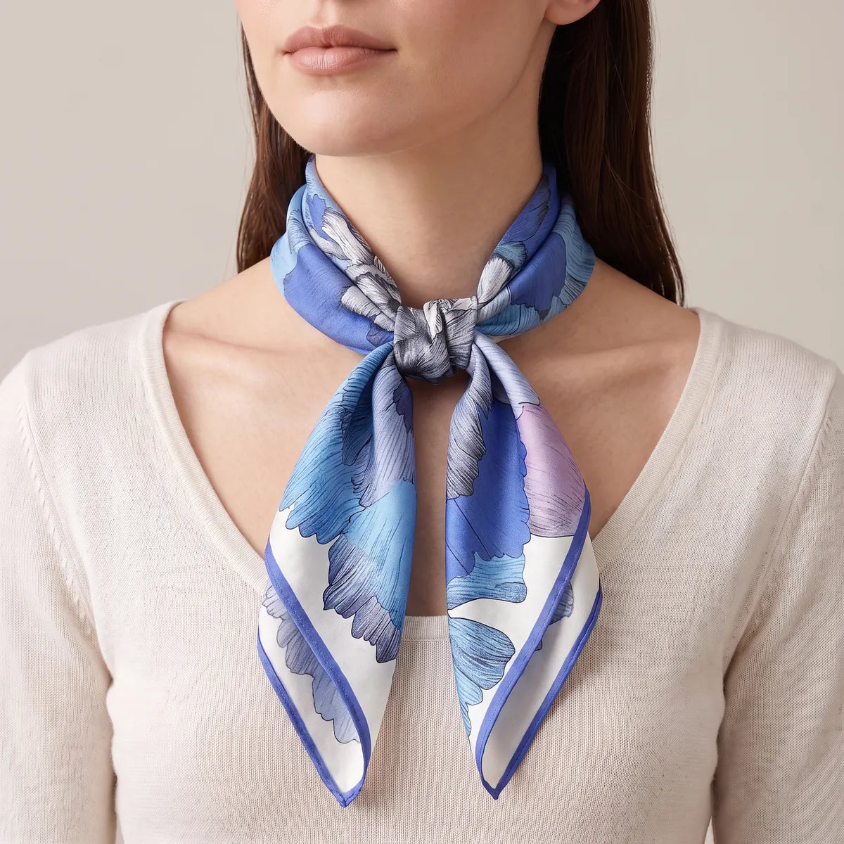 Woman in a cream sweater with the blue peony silk scarf knotted at the base of her throat