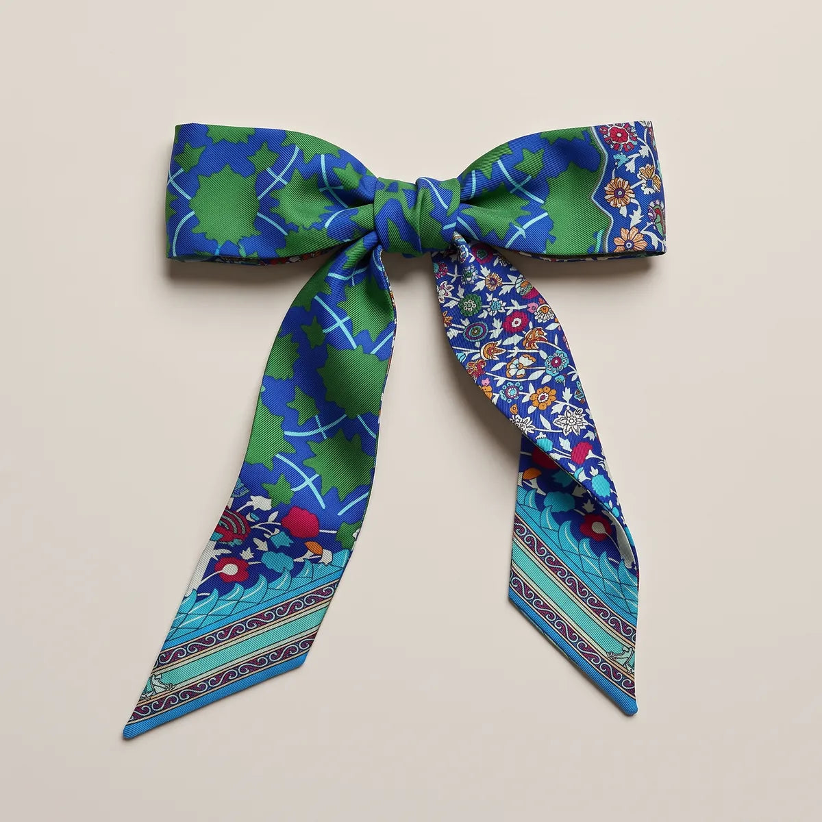 Cobalt and green skinny silk scarf tied into a flat bow, floral and leaf patterns on the two loops