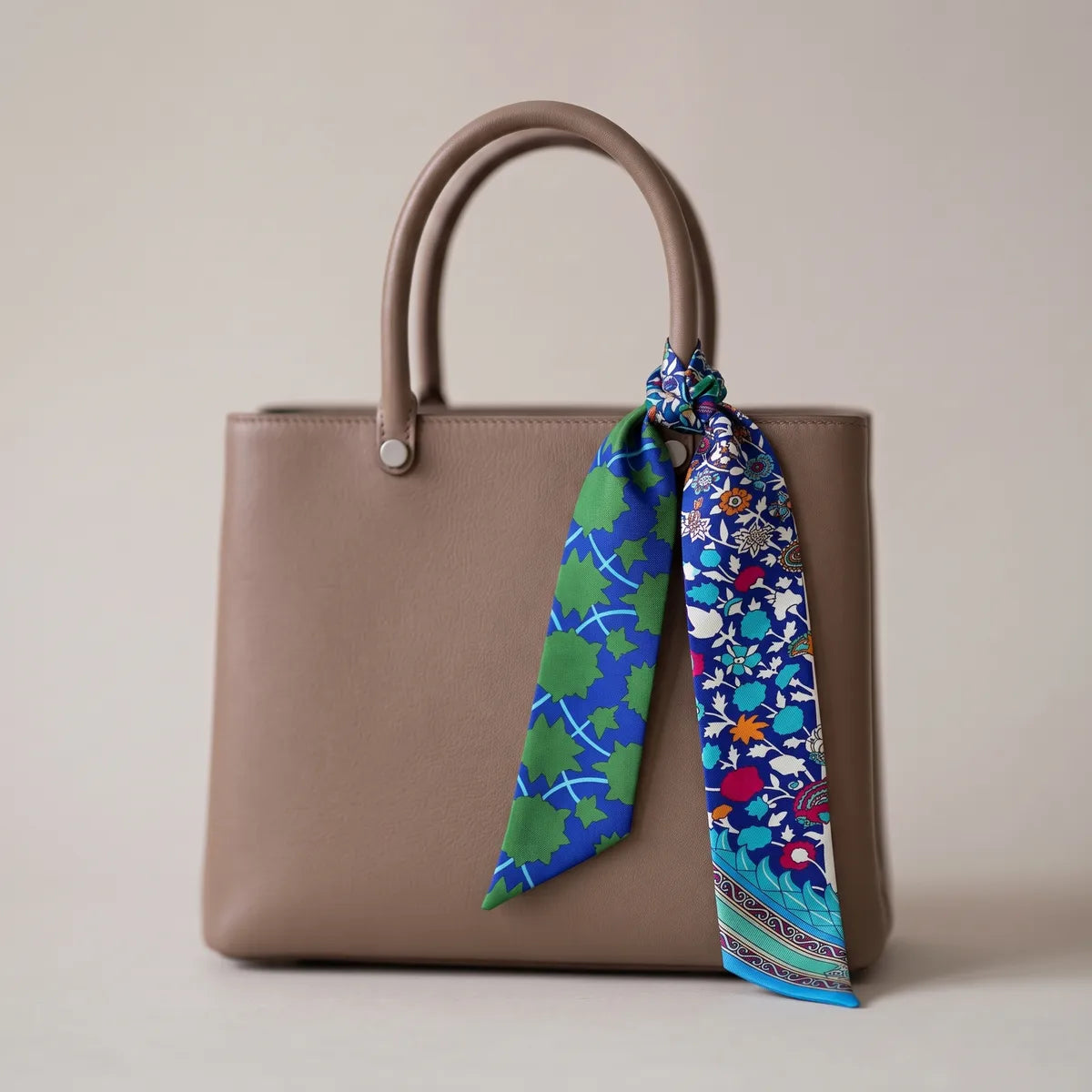 Cobalt floral skinny silk scarf knotted on the handle of a taupe leather bag, both tips hanging