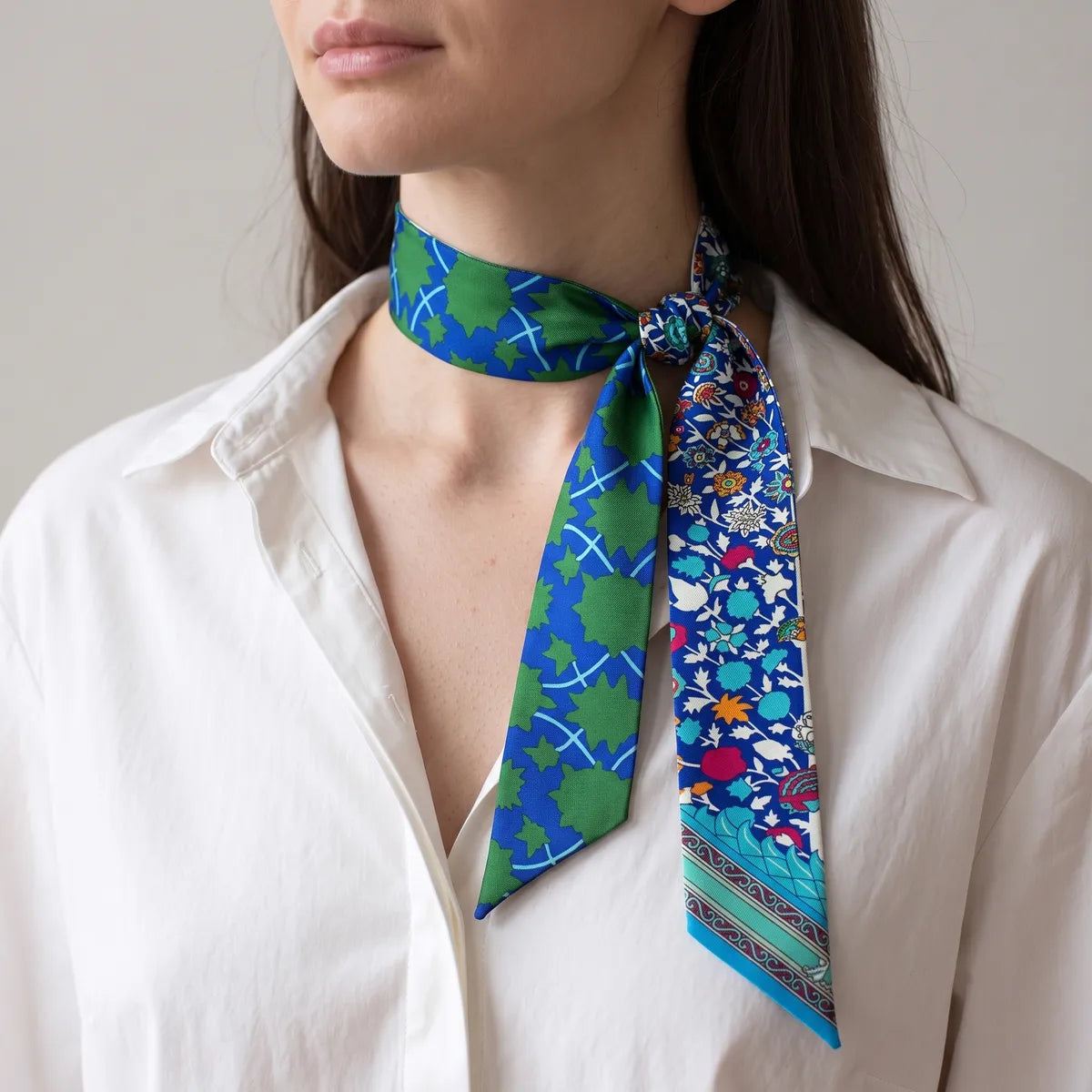 Woman in a white shirt with the blue floral skinny scarf knotted at the side of her neck, ends hanging