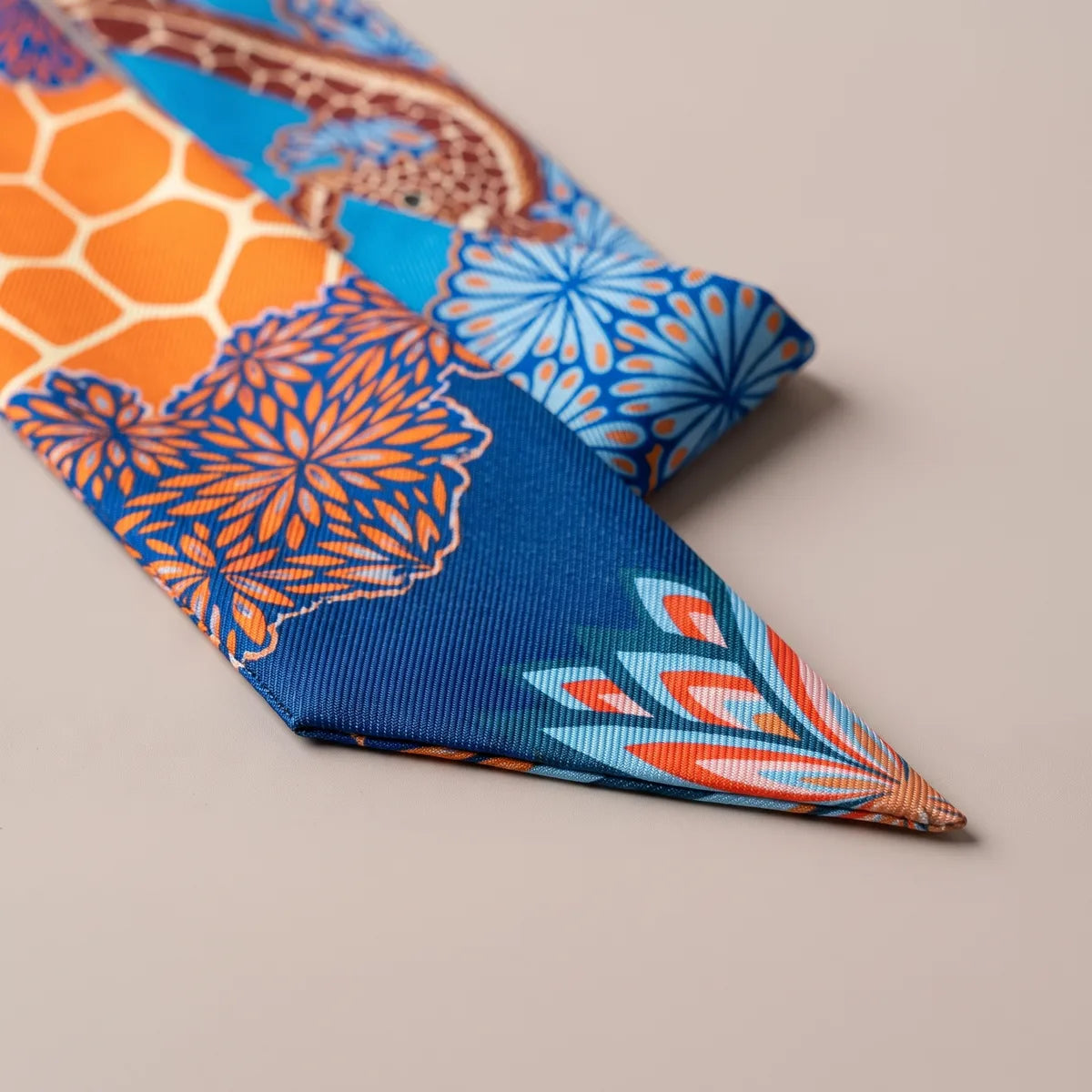 Close-up of the blue skinny scarf: blue chrysanthemums, orange honeycomb and a coral petal fan at the tip