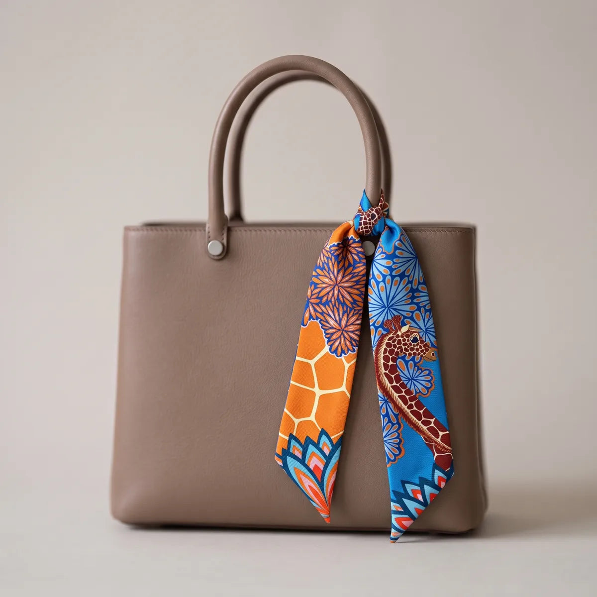 Blue giraffe print skinny silk scarf knotted around a taupe bag handle