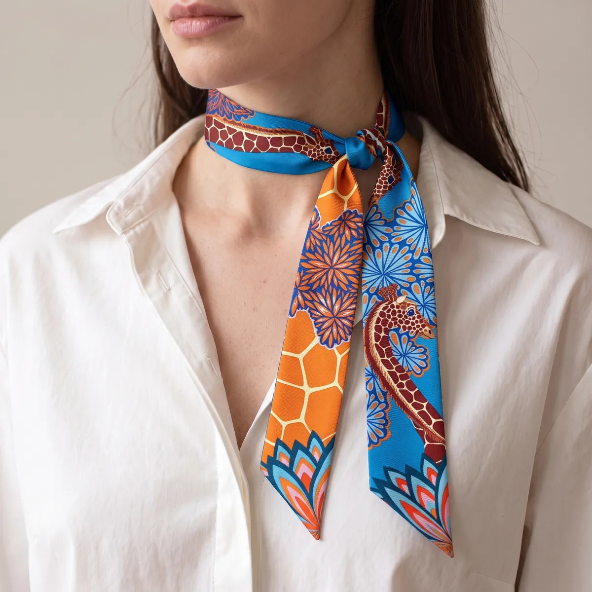 Blue giraffe skinny scarf knotted at the side of the neck over a white shirt, orange panel showing