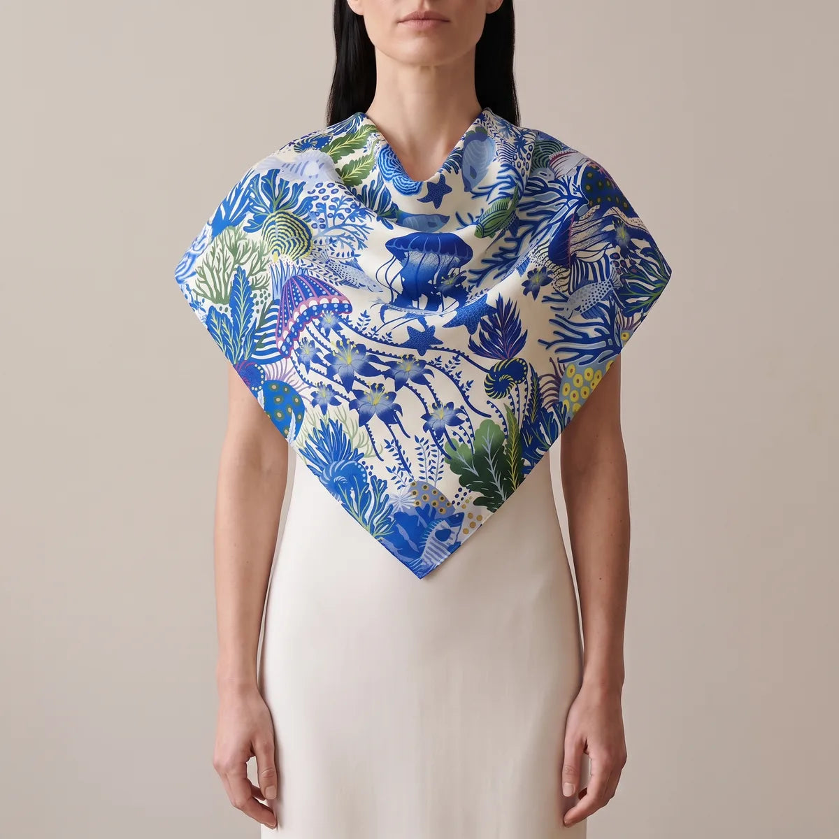 Woman wearing the blue jellyfish silk shawl over her shoulders, soft folds at the throat and a point at the front
