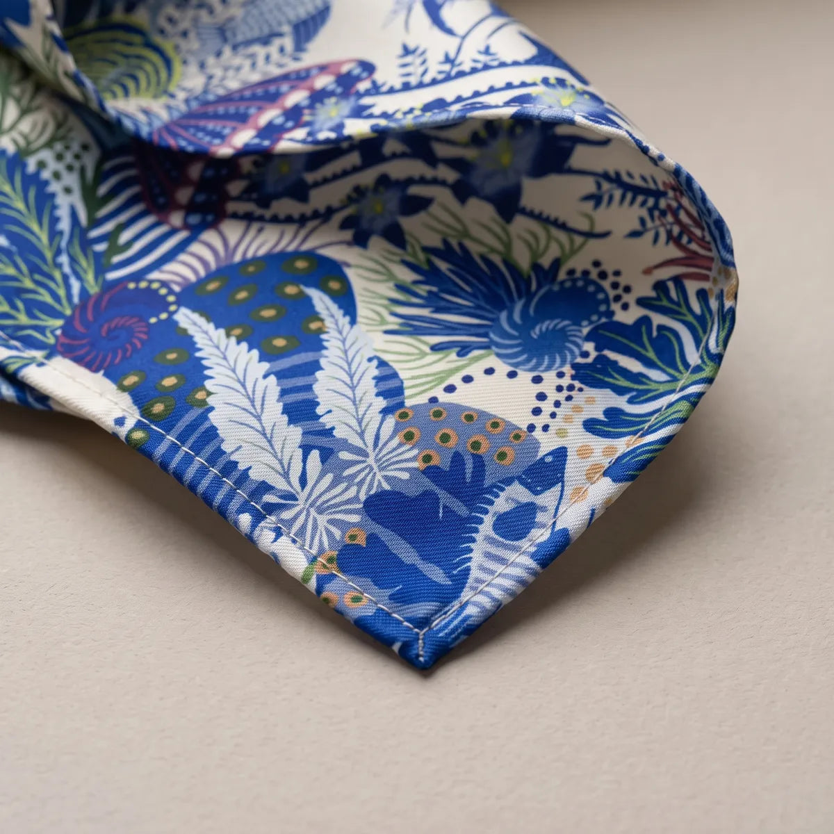 Close-up of the blue shawl's corner: pale fern-like fronds on cobalt, a spotted sea sponge and the blue hem