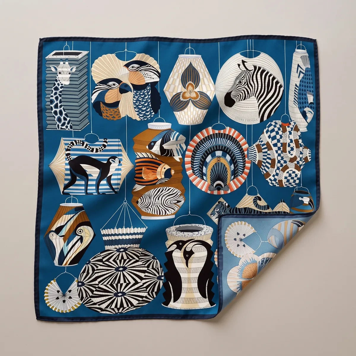 Blue lantern print silk square scarf laid flat: zebra, penguin and monkey lanterns on petrol blue, navy edge