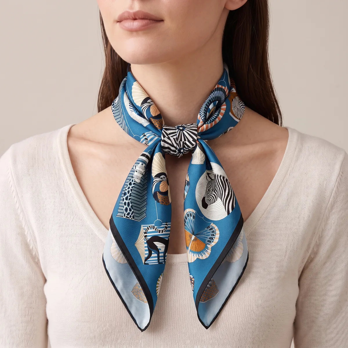Woman in a cream sweater wearing the blue lantern scarf knotted at the front of her neck