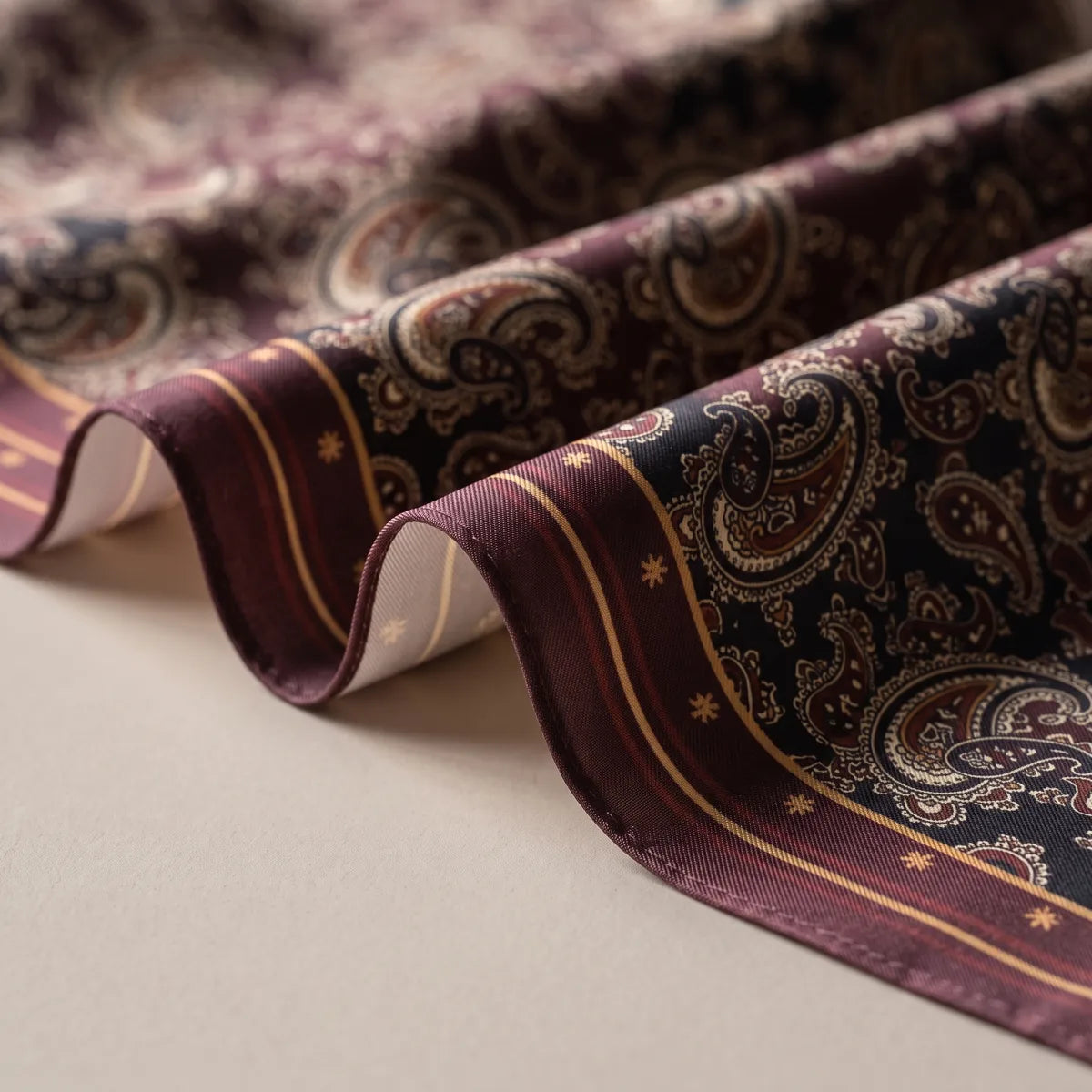 Close-up of the burgundy border on a paisley silk bandana: mustard pinstripes, small star motifs and the pale reverse