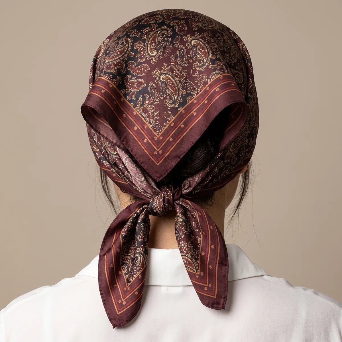 Burgundy silk scarf with a paisley print tied over the hair and knotted at the nape