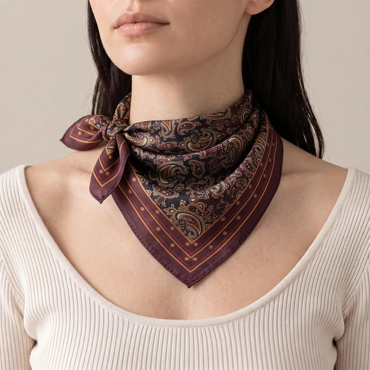 Woman wearing a burgundy paisley bandana knotted at the side of the neck over a cream ribbed top