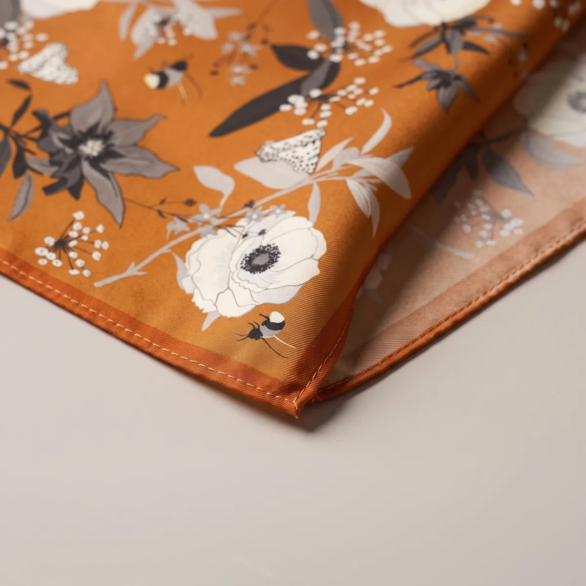 Corner of the burnt orange bandana: gray lily, white flower sprays and a bumblebee near the hem