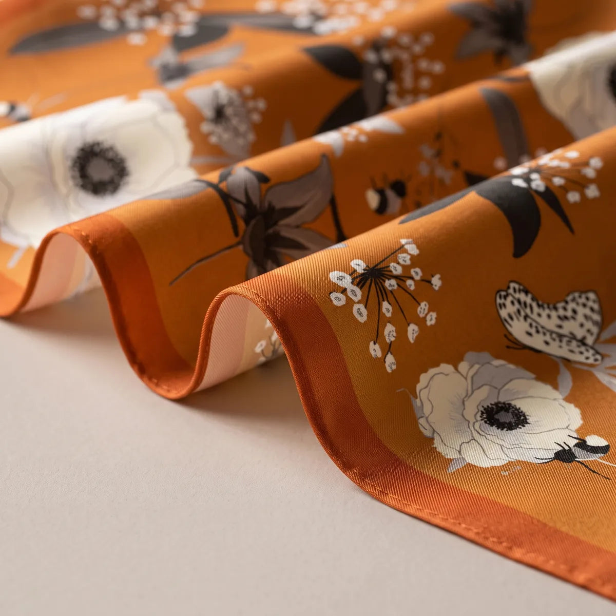 Burnt orange bandana in soft folds, close view of an anemone, a bee and the orange border