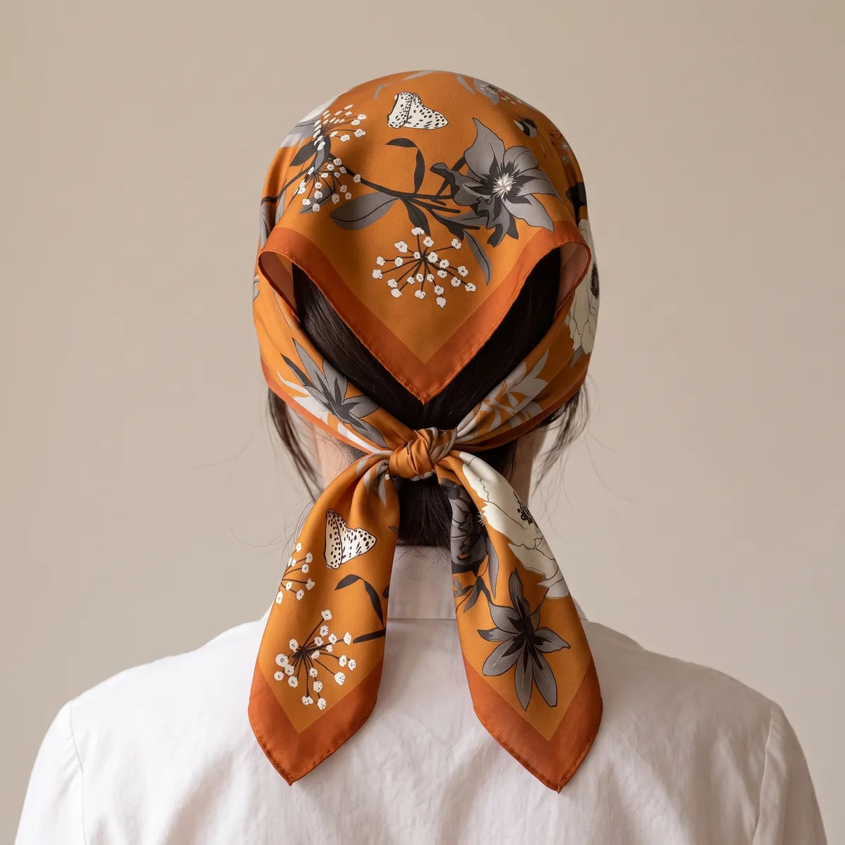 Burnt orange floral bandana tied over the hair at the nape, ends hanging, back view