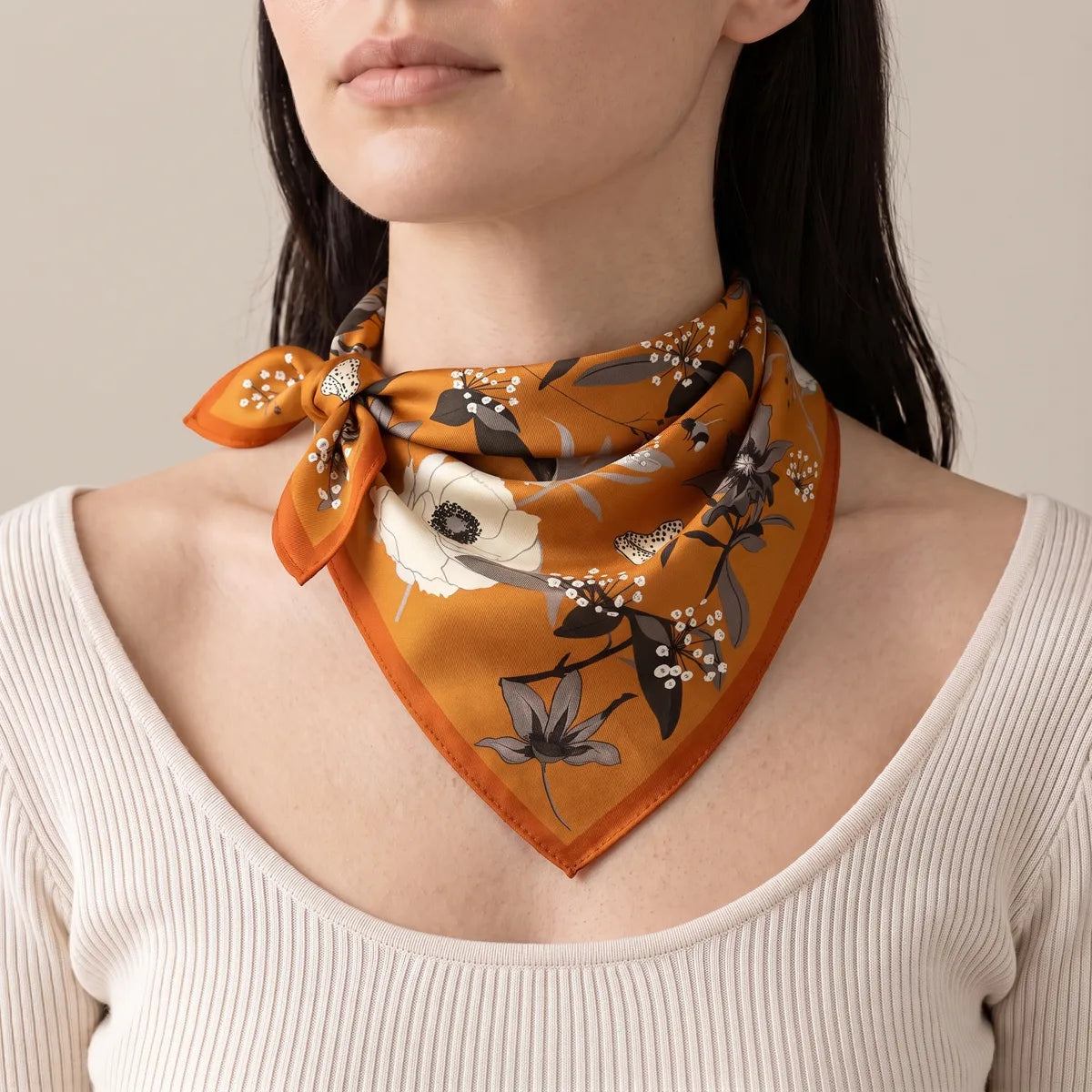 Burnt orange floral bandana knotted at the side of the neck over a cream knit top