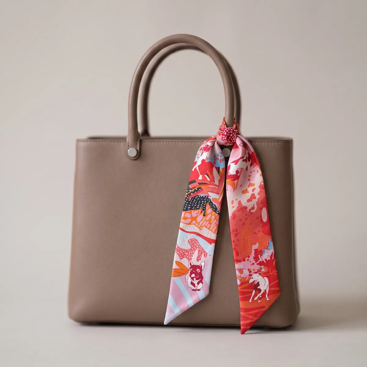 Coral dog print skinny silk scarf knotted to the handle of a taupe bag