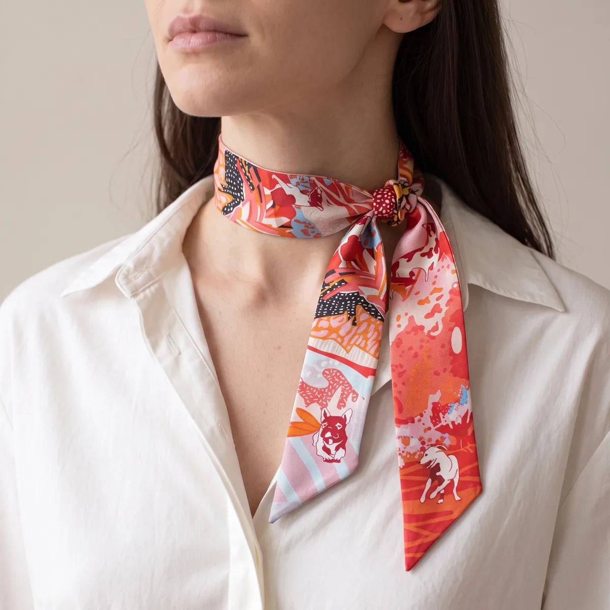 Coral dog print skinny scarf tied at the neck with the knot to one side, over a white blouse