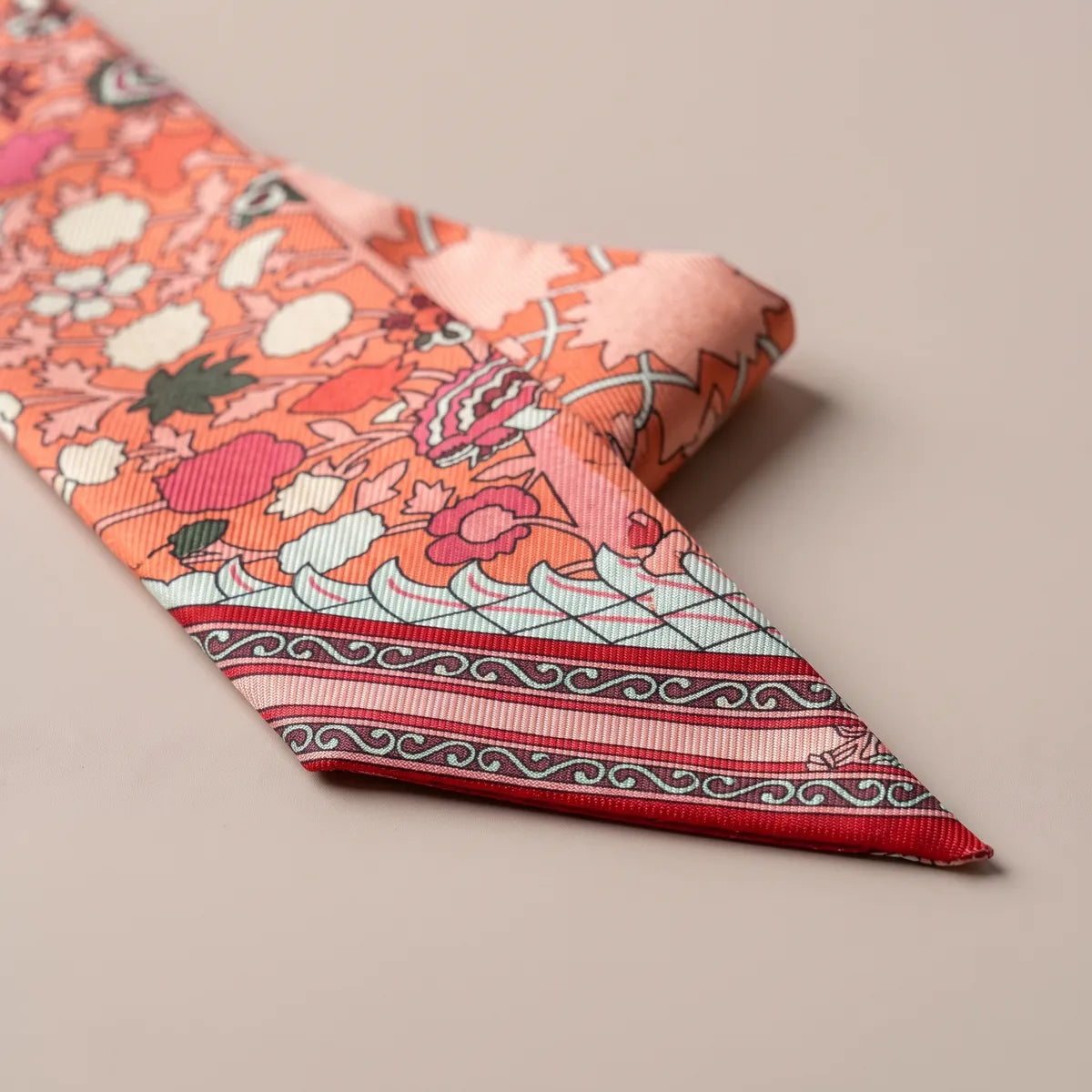 Close-up of the coral skinny scarf's slanted tip: wave scrolls and thin pink, gray and red stripes