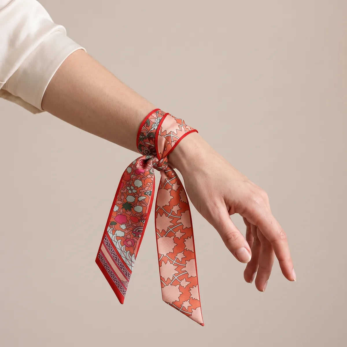 Coral and blush skinny silk scarf wound around the wrist and tied in a knot