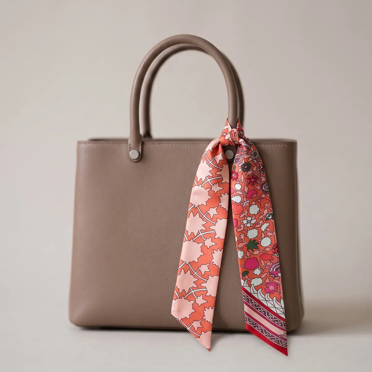 Coral floral skinny scarf tied to the handle of a taupe tote, its red-striped tip hanging