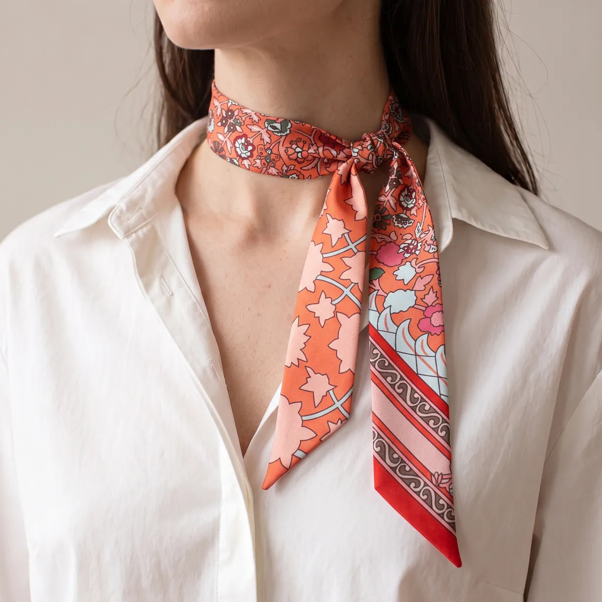 Coral floral skinny scarf knotted at the collar of a white shirt, the red-striped end falling down the front