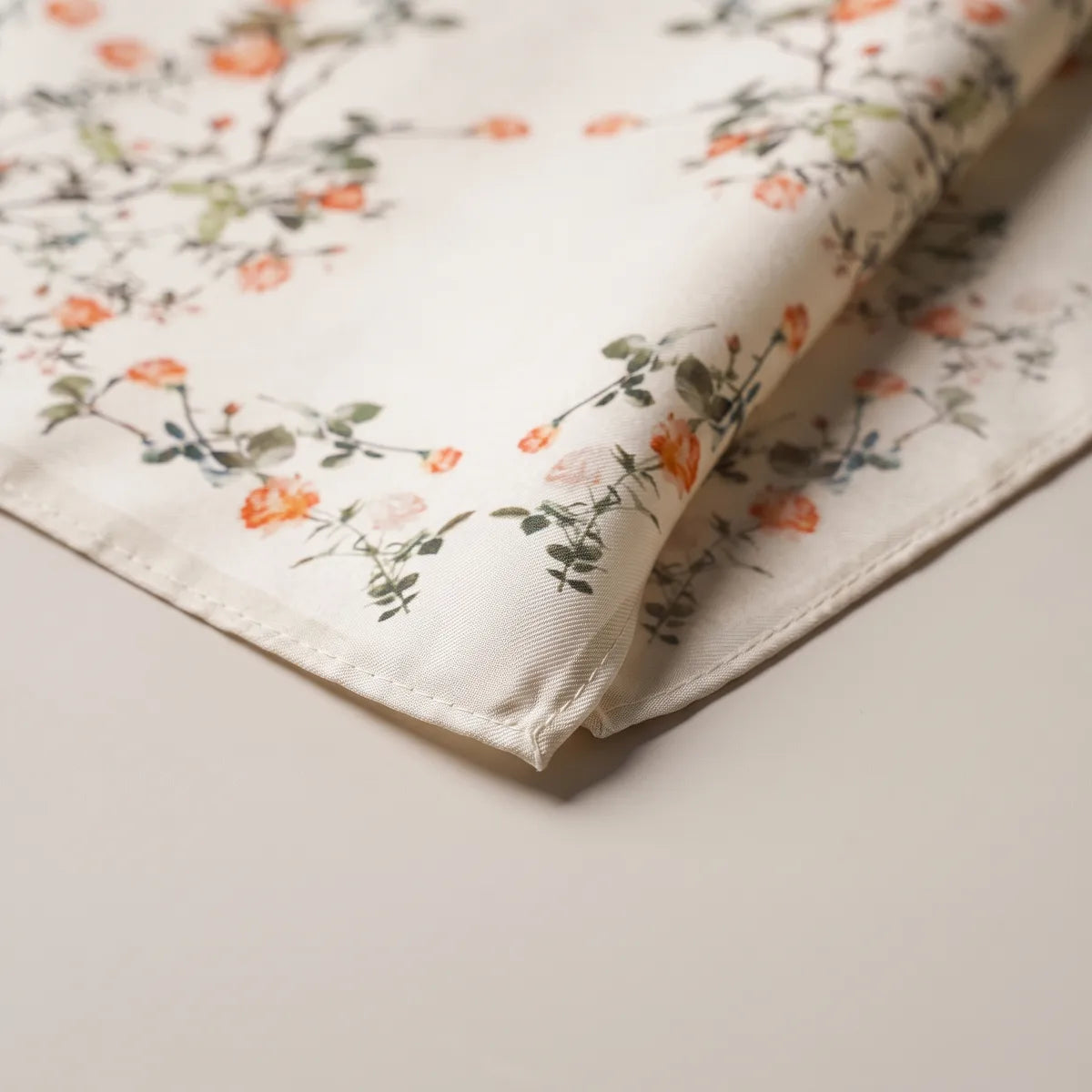 Stitched corner of the cream blossom bandana, small coral flowers and green leaves close up