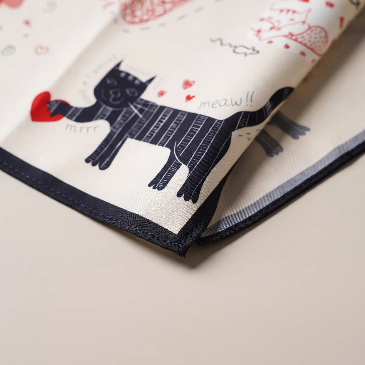 Corner of the cream cat bandana: a striped navy cat holding a red heart, handwritten words around it
