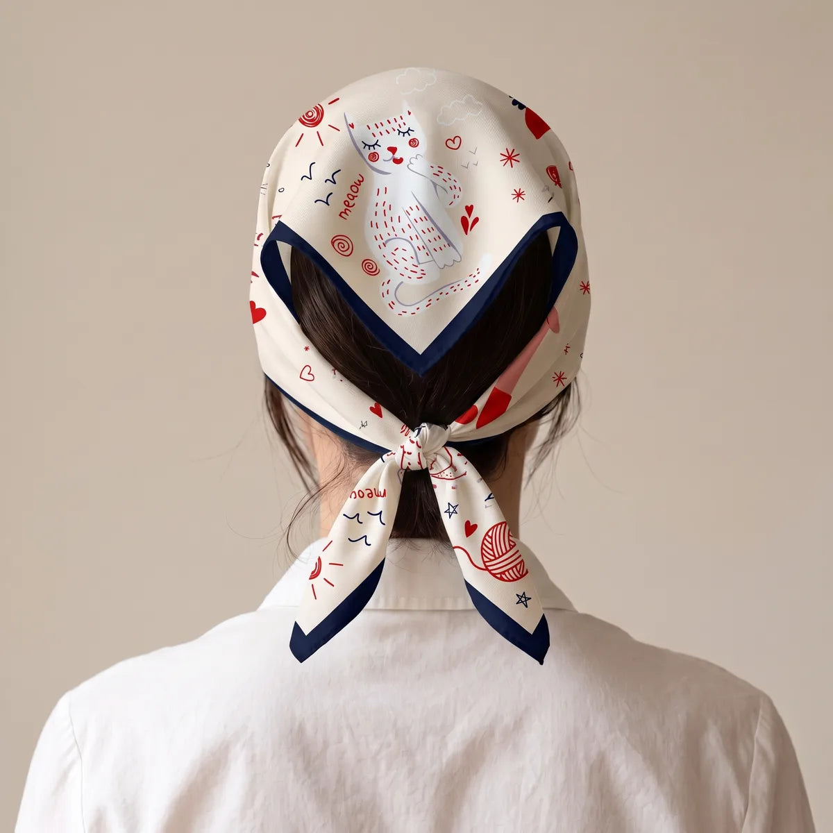 Cream cat print bandana worn as a head kerchief, knotted at the nape, seen from behind