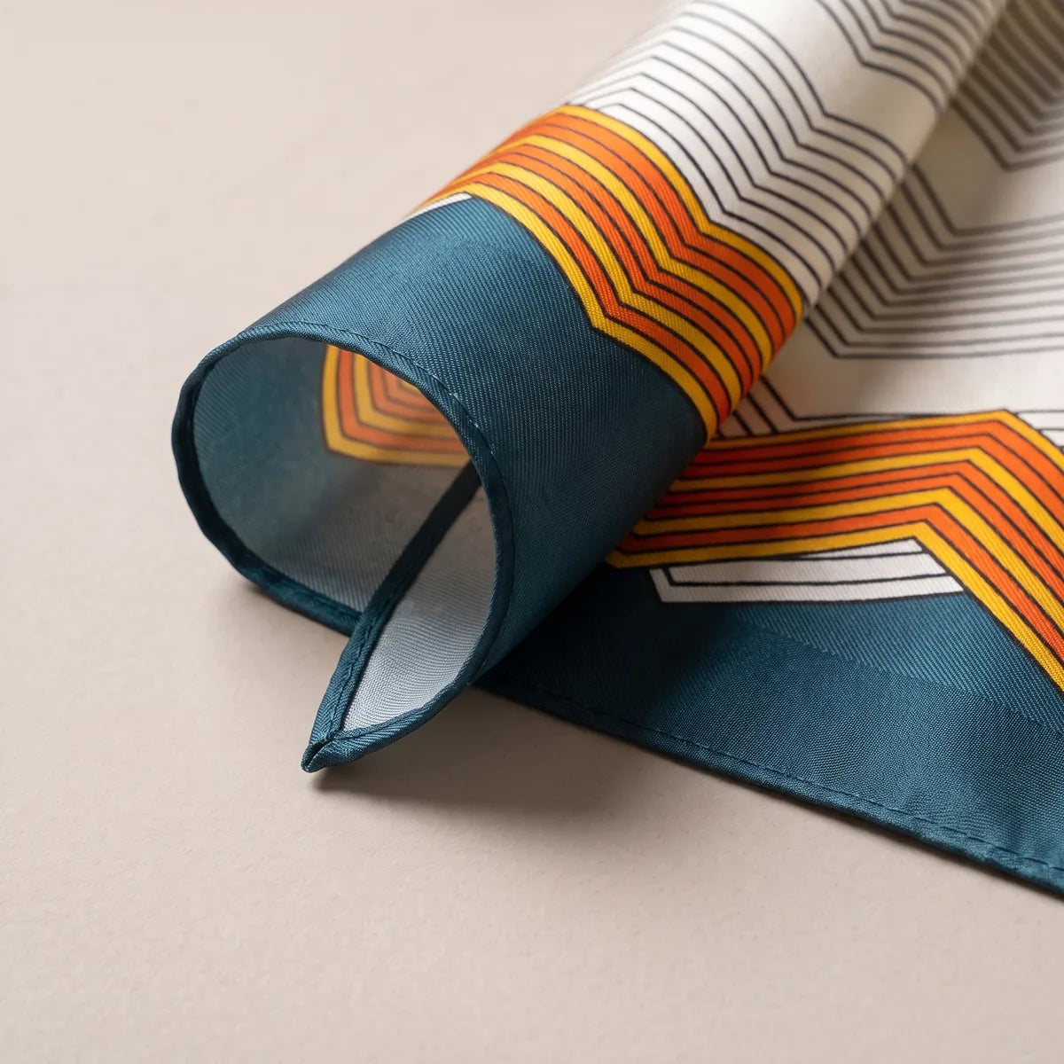 Rolled corner of the chevron scarf showing the teal band, orange stripes and a pale reverse