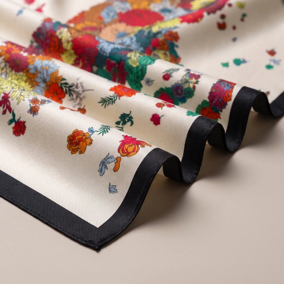 Black border rippling around scattered red, orange and blue flowers on cream silk