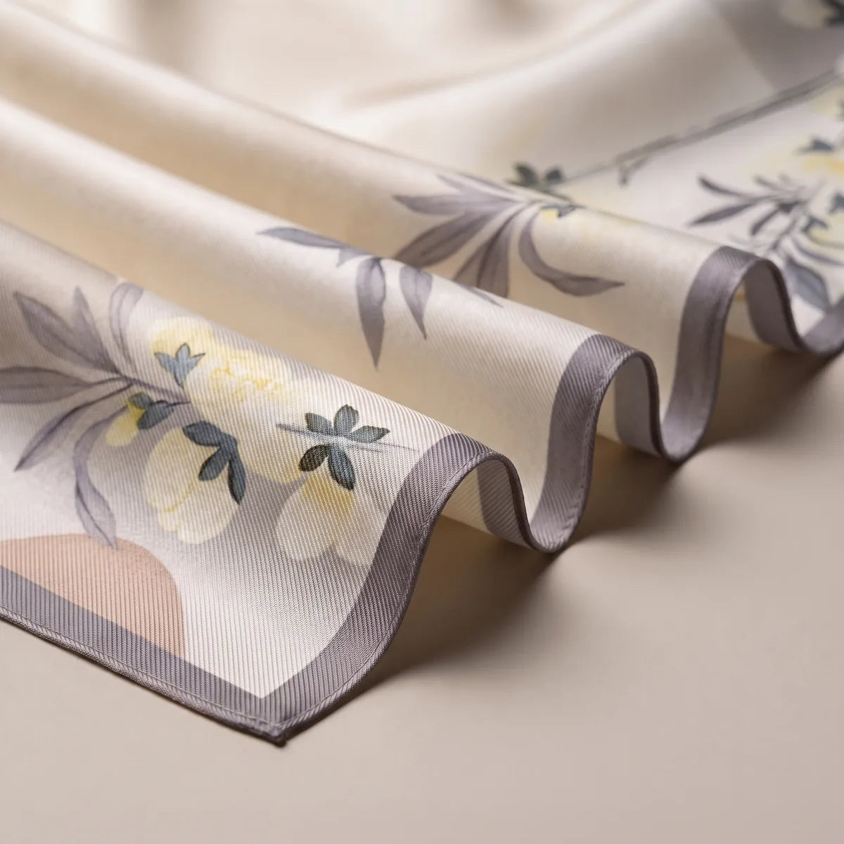 Waves of the cream floral scarf showing its gray border, lavender leaves and a pale yellow blossom