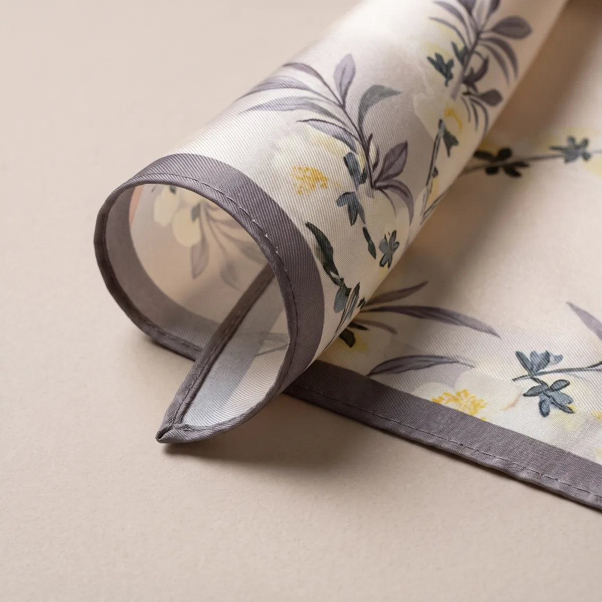 Rolled corner of the cream silk square: gray edge, blue-gray leaves and the paler print on the reverse