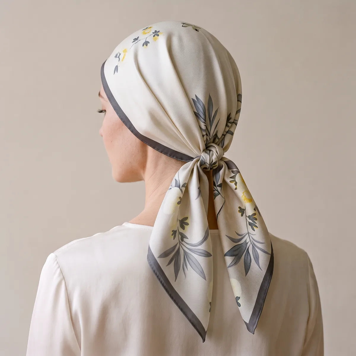 Floral silk square worn over the head, seen from behind, knotted at the nape with gray-edged tails
