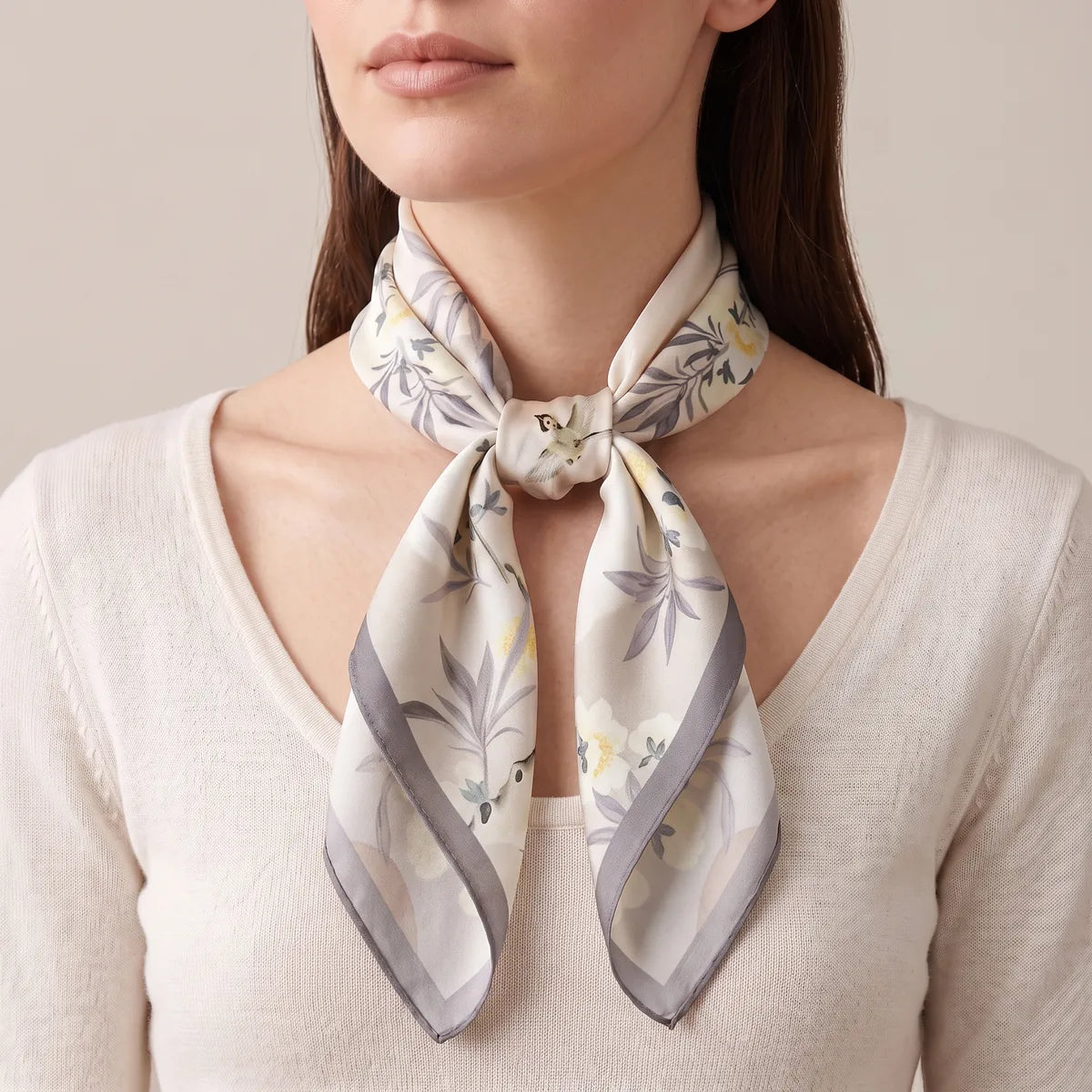 Woman in a cream sweater with the floral silk square knotted at the front of her neck, two long ends hanging