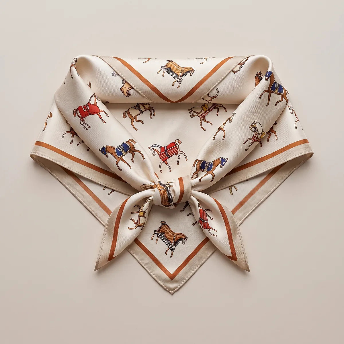 Horse print silk square folded into a knotted triangle, small red and navy horses on the tails