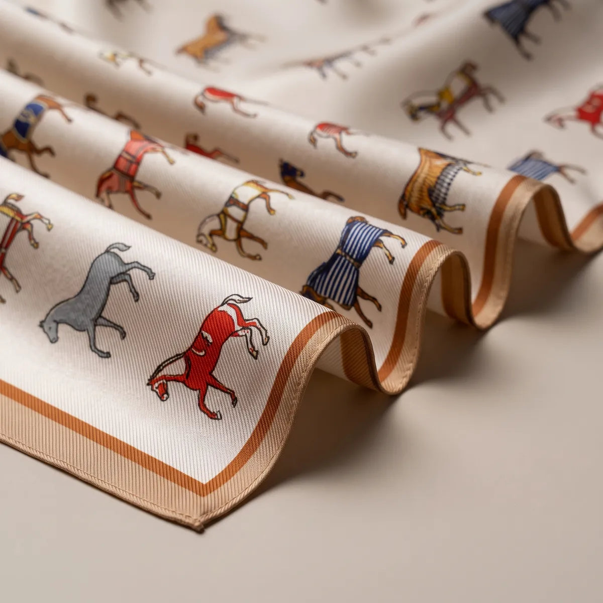 Close-up of cream silk folds: a red horse, a gray horse and the camel striped border