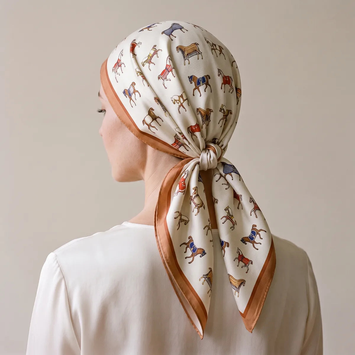 Horse print silk square covering the hair, knotted at the nape, camel border framing the face