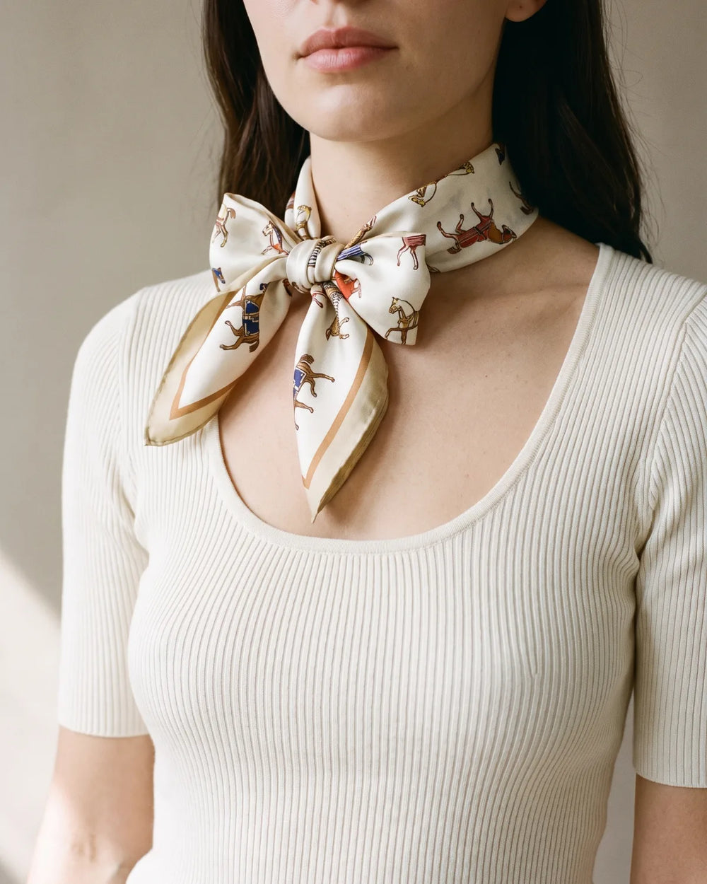 Cream horse print small silk square scarf tied in a bow at the neck
