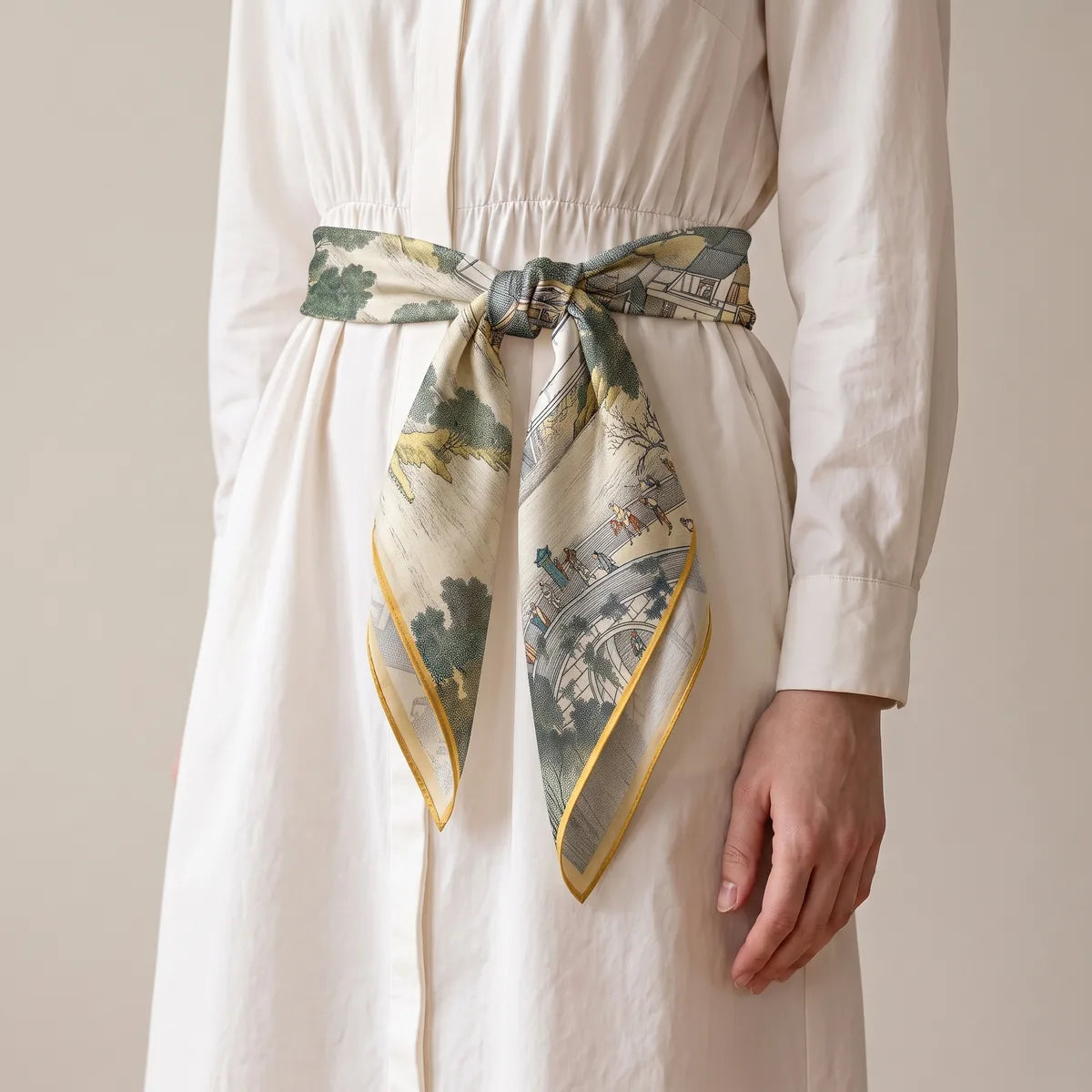 Cream landscape silk scarf tied at the waist of a white shirtdress, trees and the stone bridge on the hanging ends