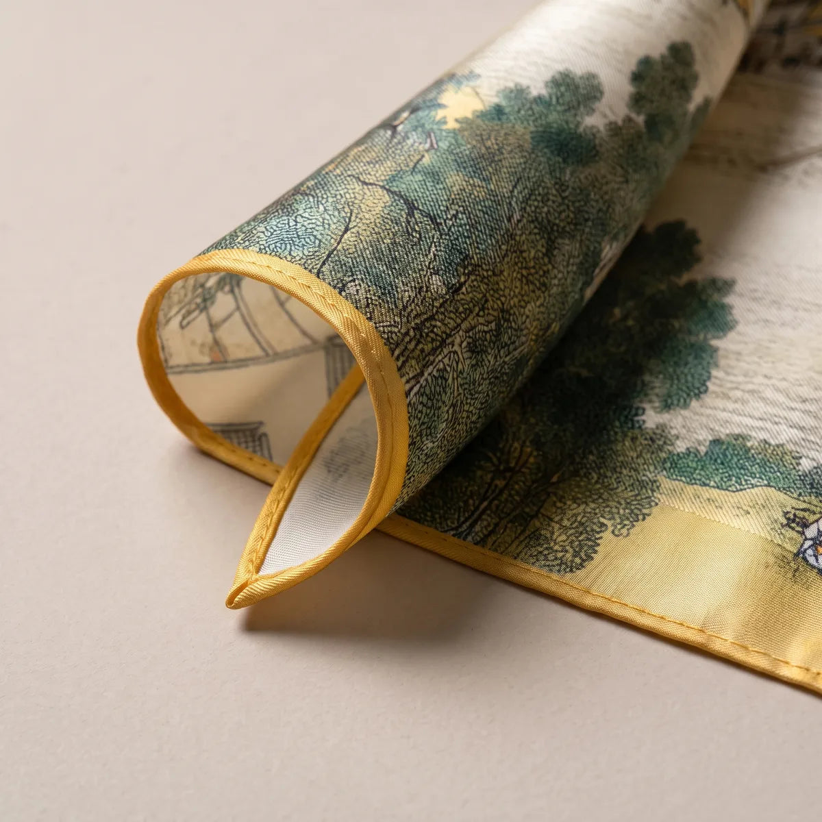 Curled corner of the village scarf: dark green trees, ink-drawn roofs and the narrow mustard hem