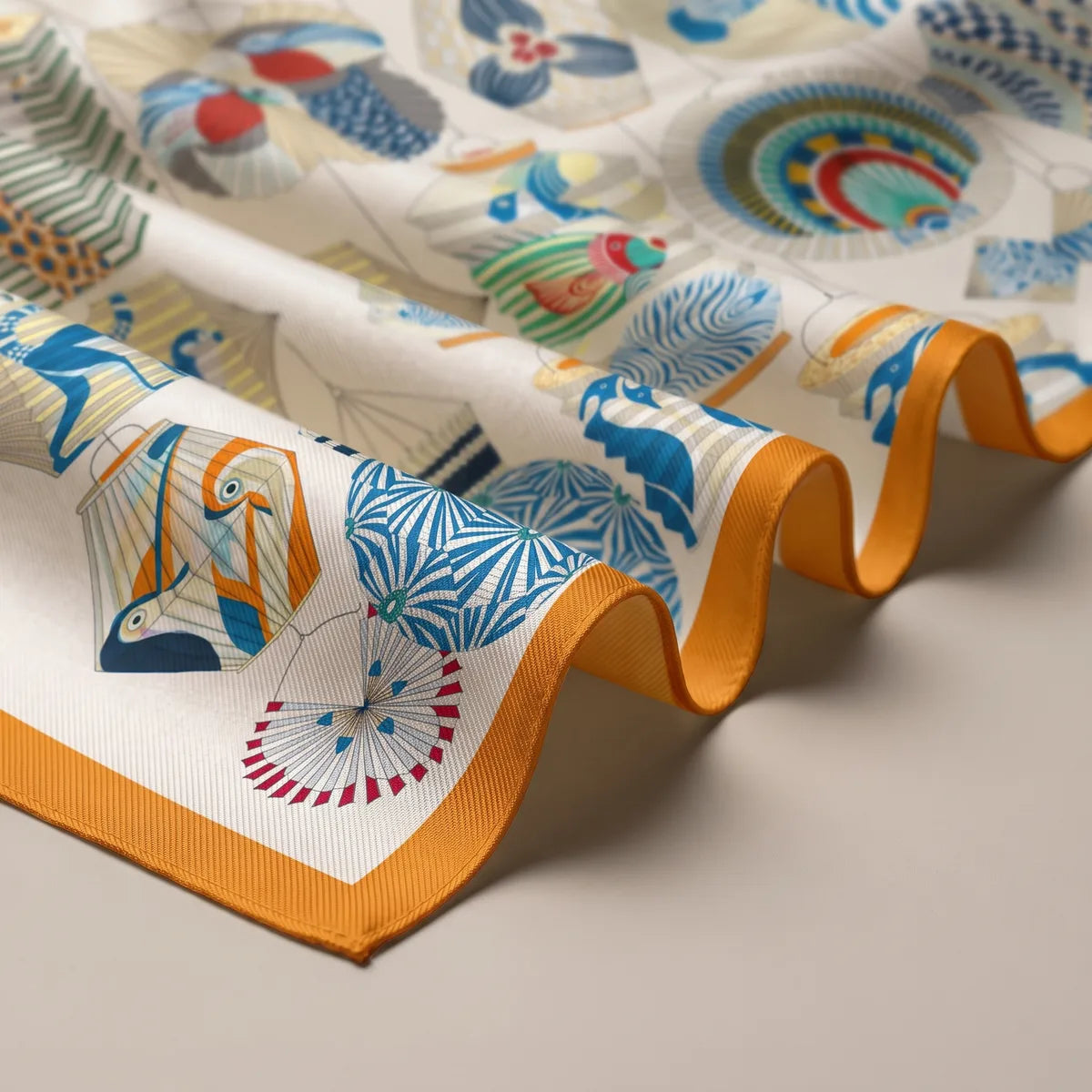 Folds of the cream silk scarf: a blue starburst lantern, a fish and the bright orange border