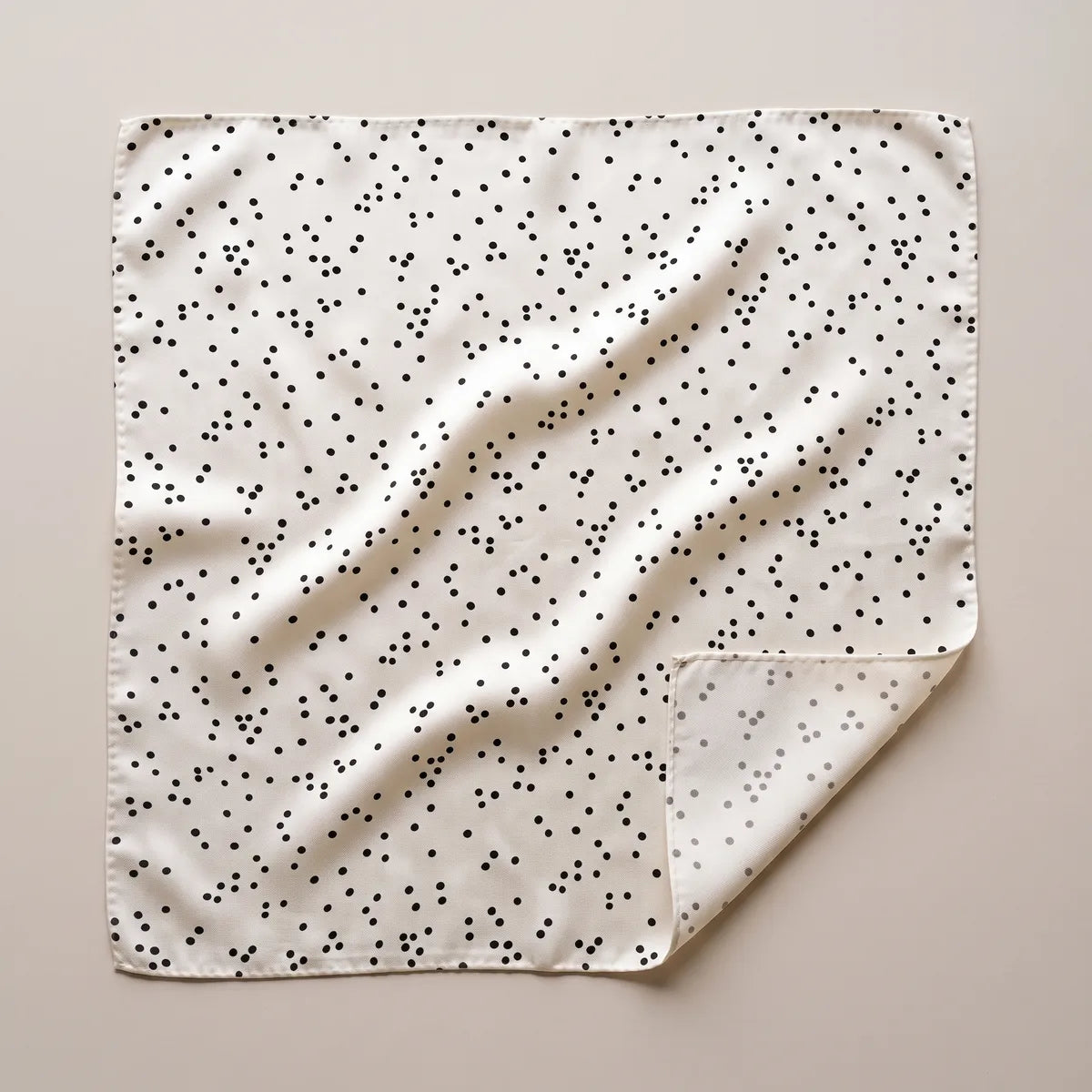 Cream polka dot silk square scarf laid flat: small black dots in loose clusters, one corner folded to a faint reverse