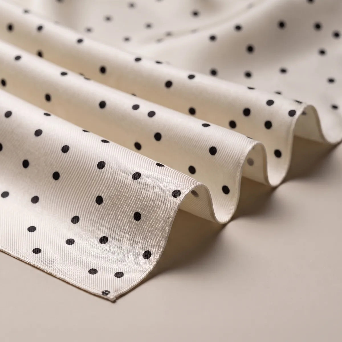 Soft folds of cream silk with scattered black polka dots and a plain cream hem